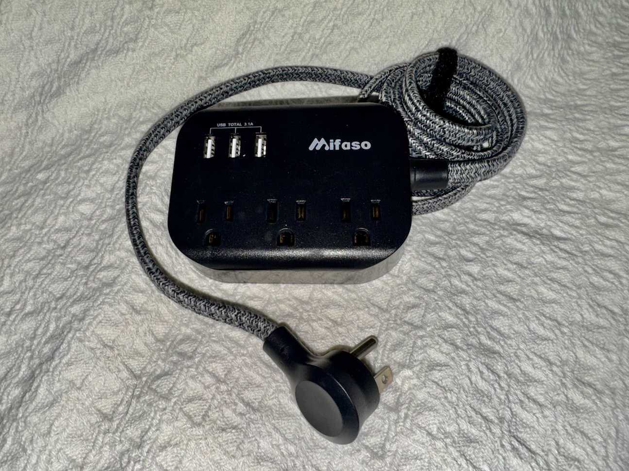 Image of a black cruise-safe power strip with multiple outlets and USB ports, specifically designed for cruise ship use. The power strip is compact and features a white or black casing with no surge protection, making it compliant with cruise line regulations. It includes several standard outlets and a few USB charging ports, allowing for the simultaneous charging of various devices like phones, tablets, and cameras while on board. The power strip is shown placed on a flat surface, with its features clearly visible.