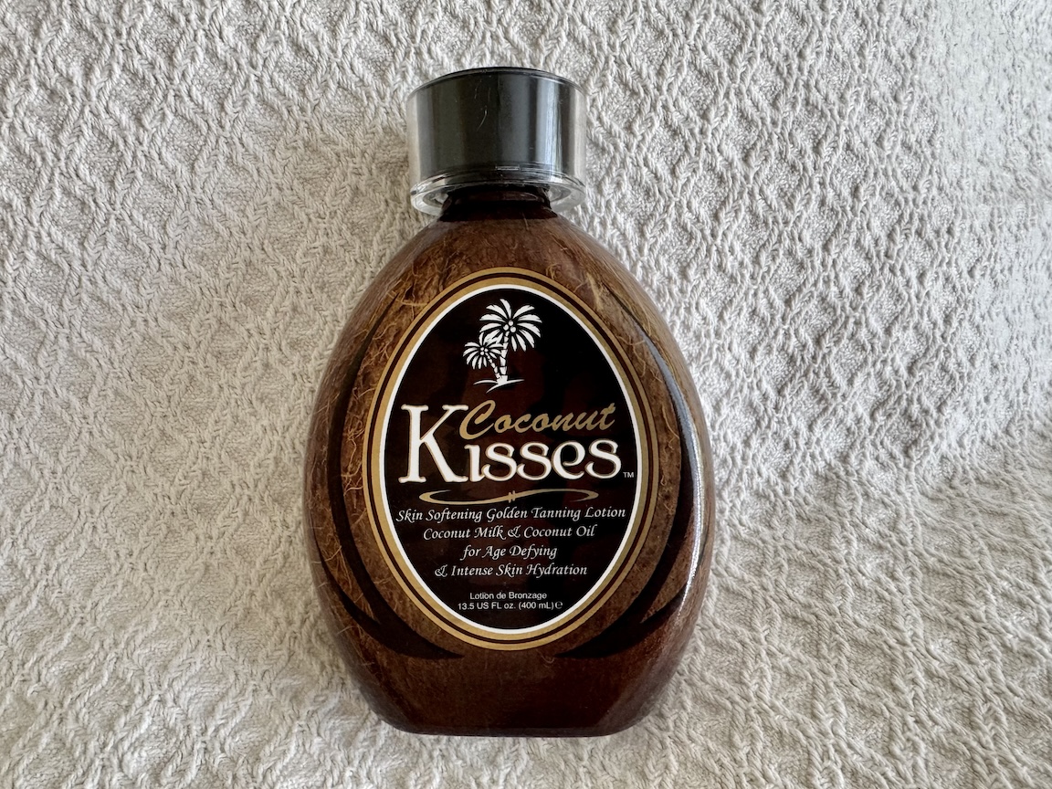 Image of two bottles of Ed Hardy Coconut Kisses Golden Tanning Lotion, each containing 13.5 oz. The bottles are designed with vibrant tropical colors and feature the Ed Hardy logo along with a stylized coconut and palm tree motif. The label highlights the lotion’s ability to enhance tanning while nourishing the skin with a blend of coconut milk and coconut oil. The bottles are shown standing side by side against a plain background, with product details and branding clearly visible.